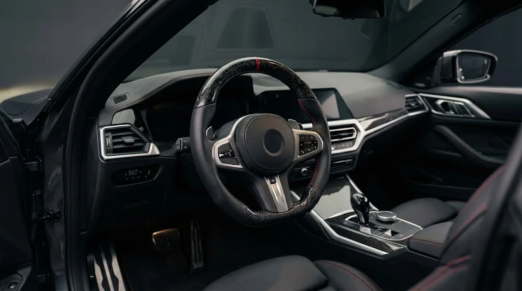 Interior view of an AKIUMI custom steering wheel for a Lexus IS with forged carbon trim, perforated black leather grips and blue stitching